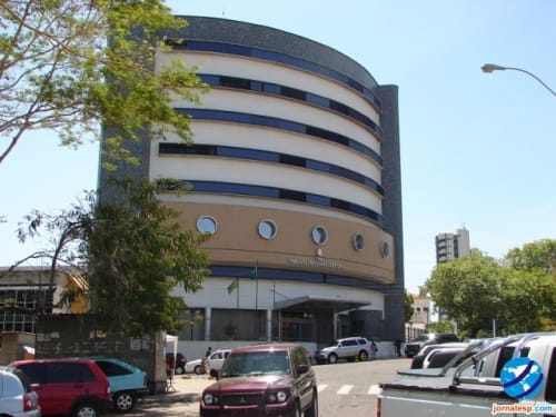 Fachada curva de prédio comercial de vários andares com janelas em faixas azuis, carros estacionados na frente
