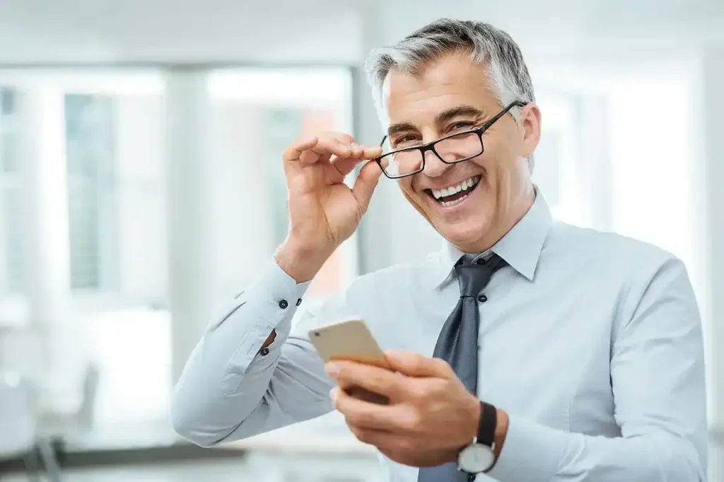 Homem elegante, bem vestido, sorrindo e segurando uma embalagem de presente personalizada.