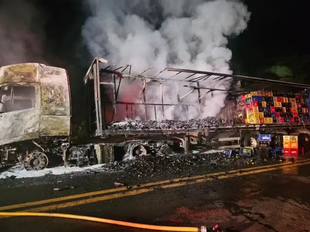 Carreta com carga de cerveja pega fogo e tem parte da estrutura destruída em Monsenhor Gil 9 Vista noturna de uma carreta em chamas na zona rural de Monsenhor Gil, com bombeiros trabalhando para apagar o fogo que consome a cabine e parte da carga de cerveja.