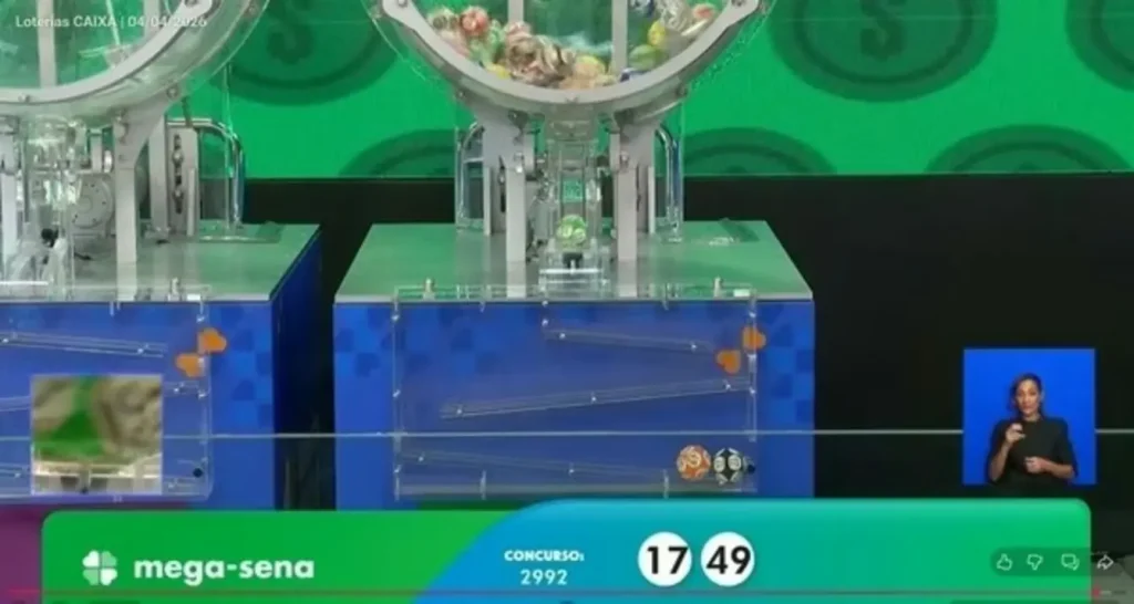 Mão de uma pessoa segurando uma caneta e preenchendo um volante de aposta da Mega-Sena sobre uma mesa.