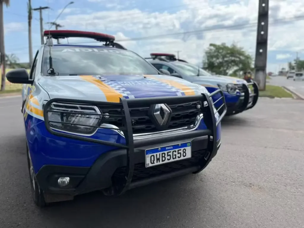Vista frontal de uma viatura da Polícia Militar, modelo Renault Duster, estacionada em uma via pública sob um céu nublado.