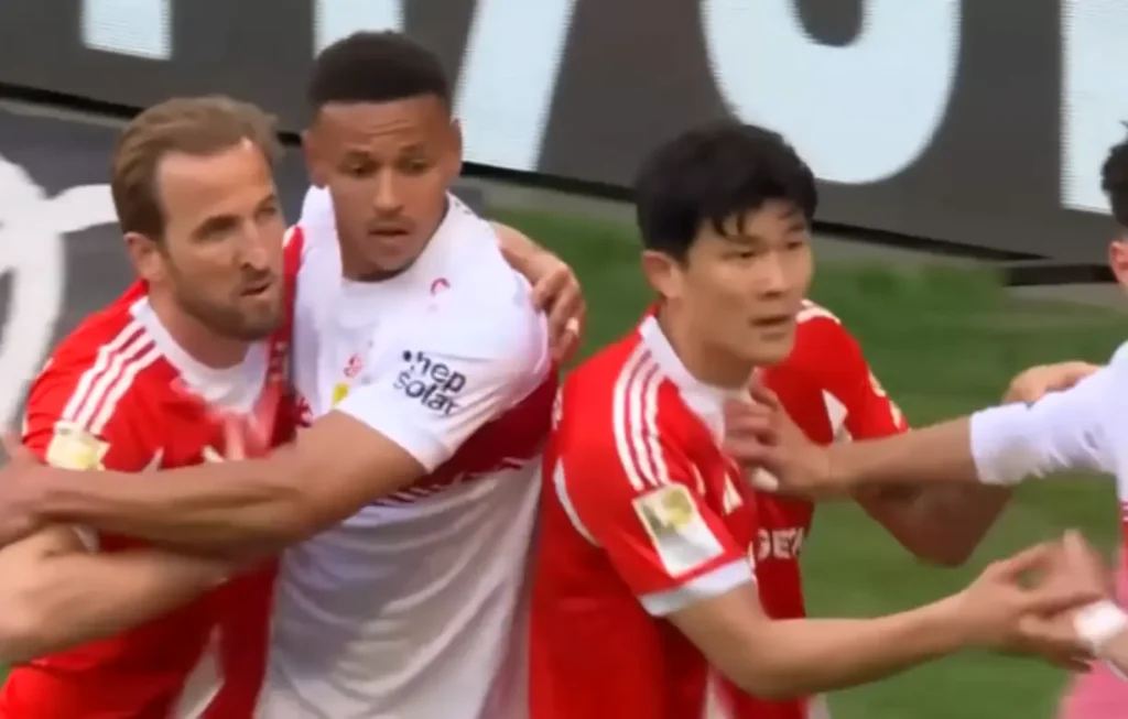 Três jogadores de futebol em disputa corporal durante partida: dois atletas com uniforme vermelho e branco seguram um jogador adversário com camisa branca e patrocínio 'hep solar', em lance de bola parada