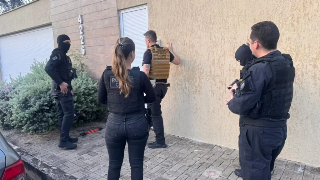 Policiais em operação na frente de uma residência, com agentes em coletes táticos e um de balaclava. Número 4226 visível.