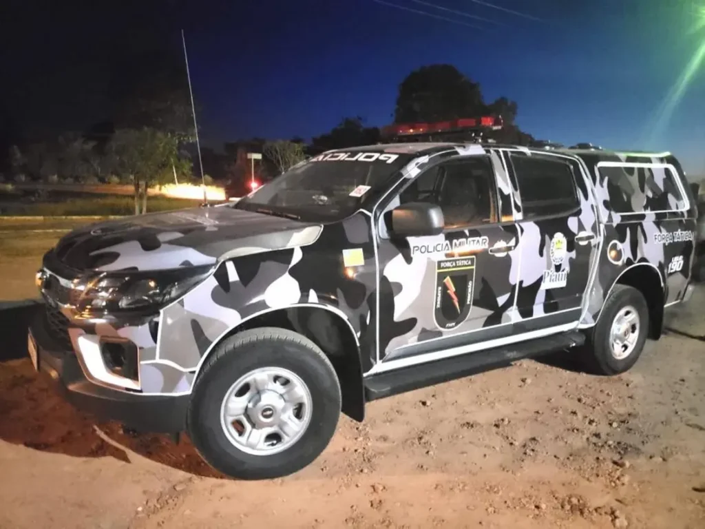 Viatura da Força Tática da Polícia Militar do Piauí, uma caminhonete S10 camuflada, estacionada em um terreno de terra à noite.