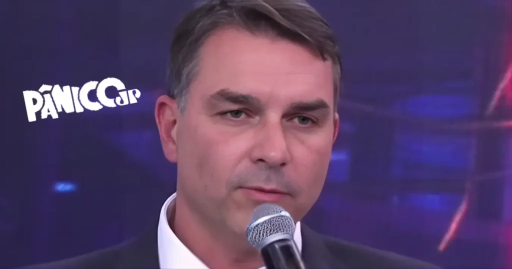 flávio bolsonaro segurando microfone durante participação no programa Pânico da Jovem Pan, com logo 'Pânico JP' visível ao fundo