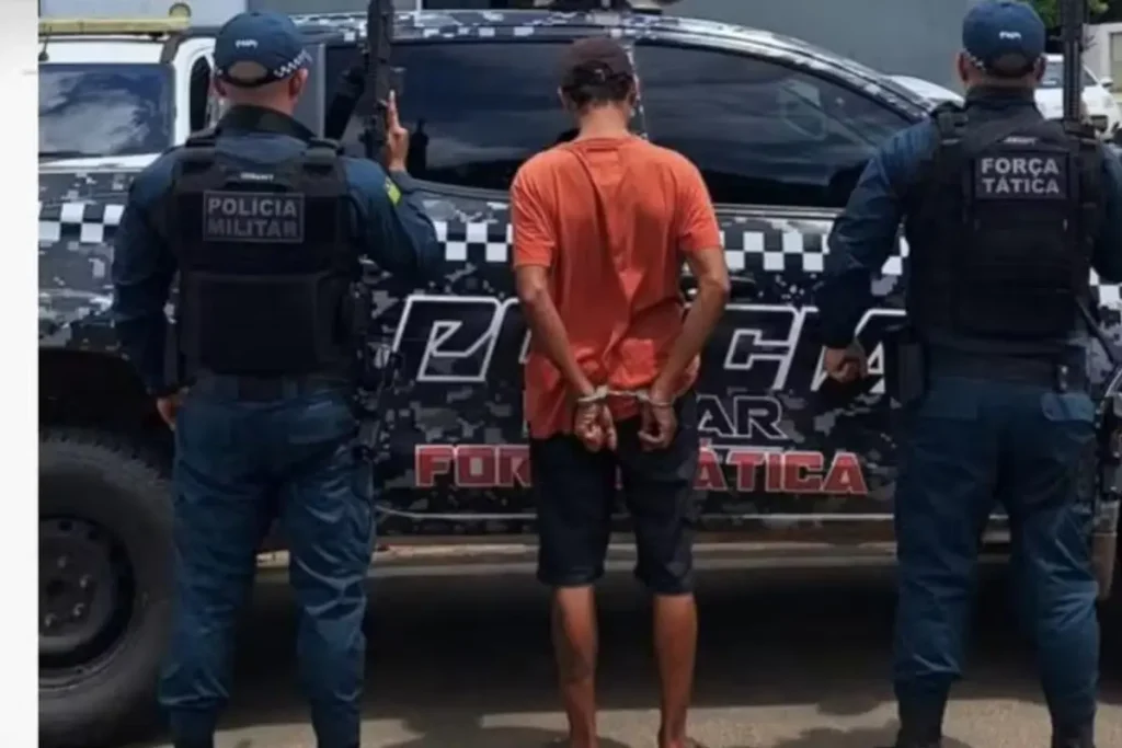 Homem de costas, algemado, sendo conduzido por policiais militares em uma área rural no Piauí.