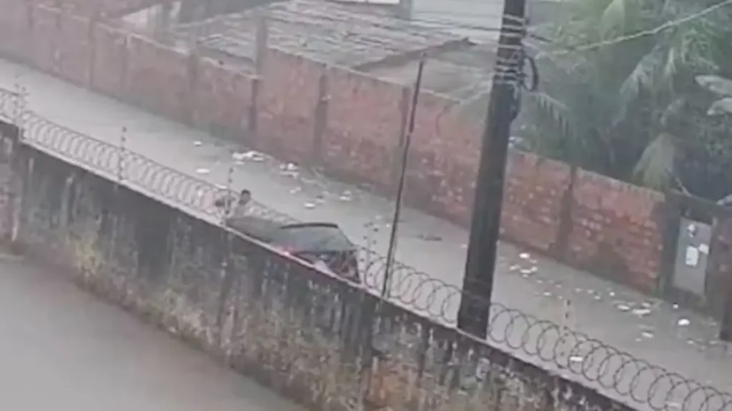 Homem empurra um carro parcialmente submerso em uma rua inundada, em imagem capturada de um ponto de vista elevado.