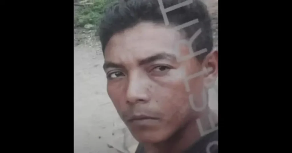 Fotografia de rosto de um homem com cabelo escuro e expressão séria, identificado como suspeito procurado pela polícia.