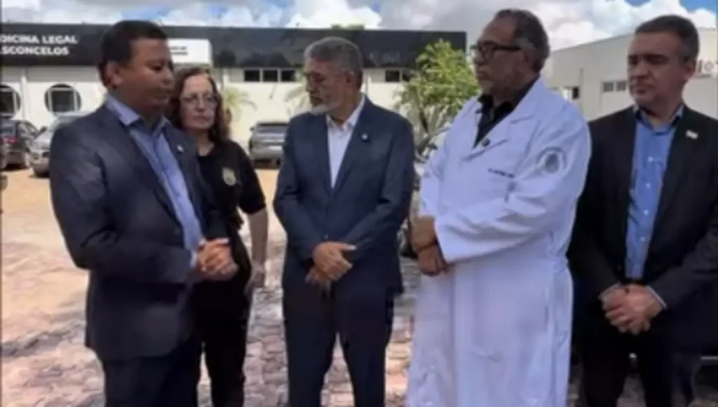 Cinco pessoas, incluindo um médico e oficiais, em frente a um prédio da Medicina Legal, em um evento formal.