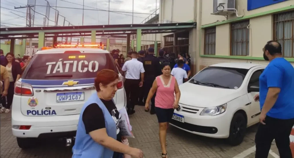 Viatura da Polícia Tático com luzes acesas e pessoas em frente a um prédio, indicando movimentação ou operação policial.
