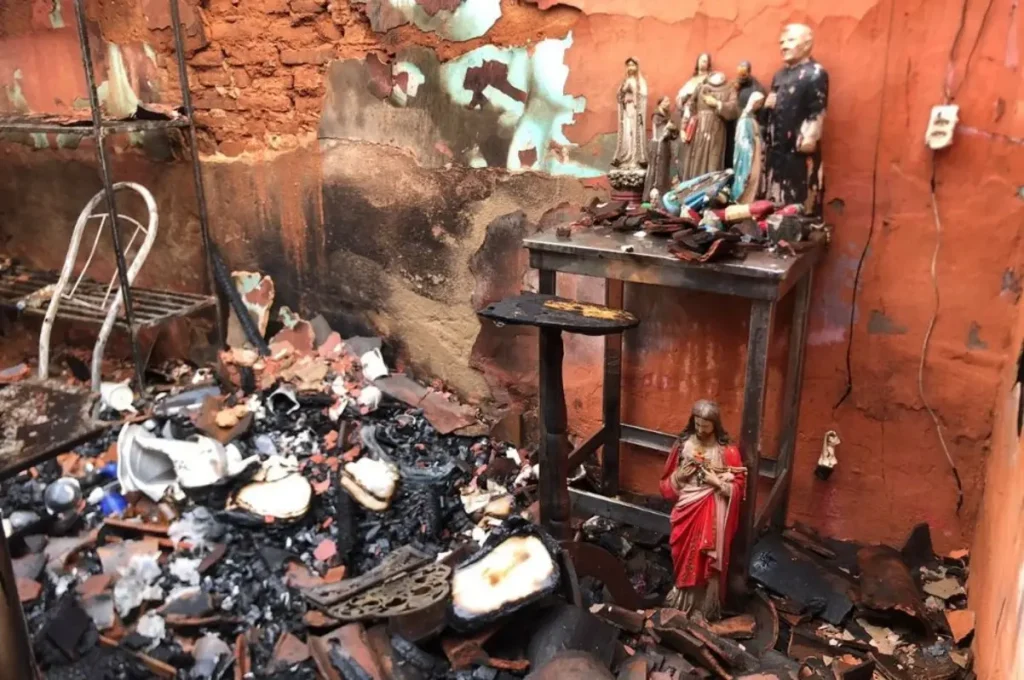 Altar com estátuas religiosas intactas em cômodo residencial destruído por incêndio, com cinzas e escombros.