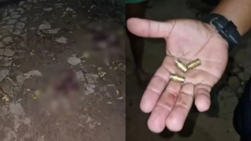 Mão segurando três cápsulas de bala e chão escuro com manchas borradas, possivelmente sangue, em cena noturna.