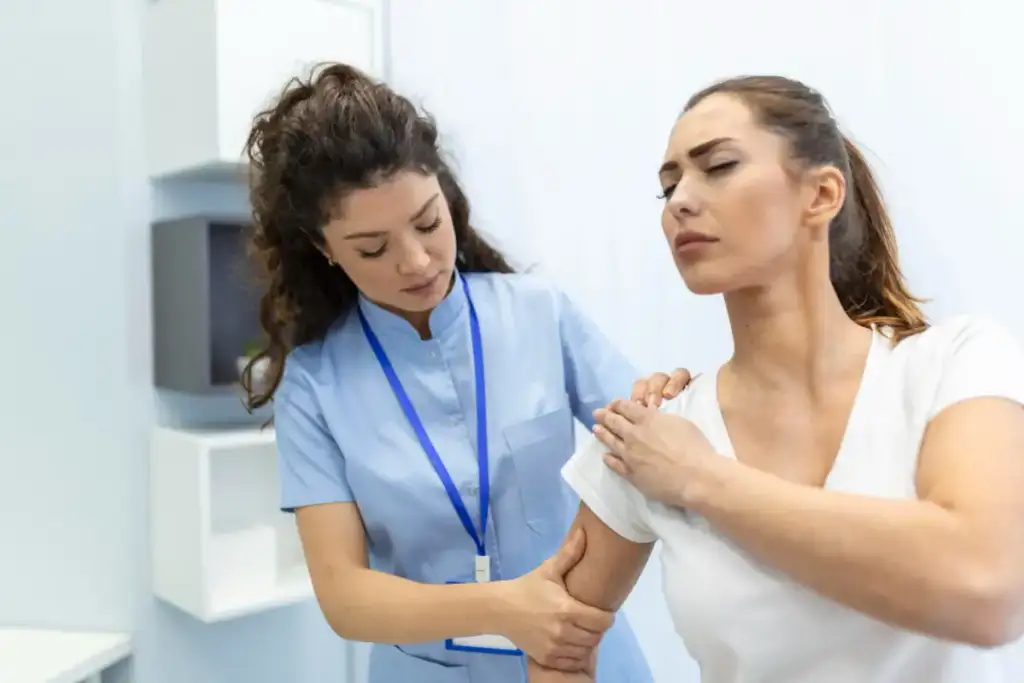 Profissional de saúde examinando o ombro de uma paciente com expressão de dor em ambiente clínico