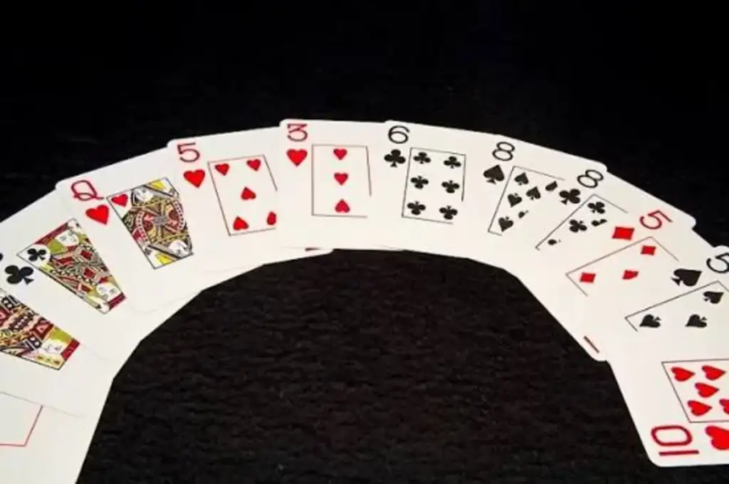 Leque de cartas de baralho dispostas em arco sobre superfície preta, incluindo Dama, 5, 3, 6, 8 e outras cartas de diferentes naipes