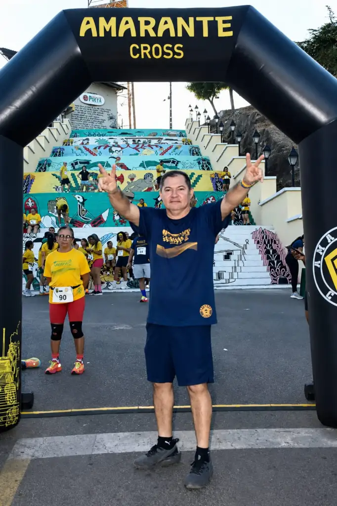 Participante celebra sob o arco inflável da 2ª Corrida do Papagaio em Amarante, com escadaria colorida ao fundo e outros atletas reunidos