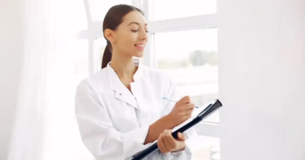 Profissional de saúde com jaleco branco sorrindo enquanto faz anotações em uma prancheta