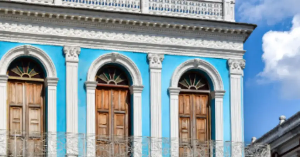 Fachada de edifício colonial azul com colunas brancas, portas de madeira em arco e sacadas de ferro forjado