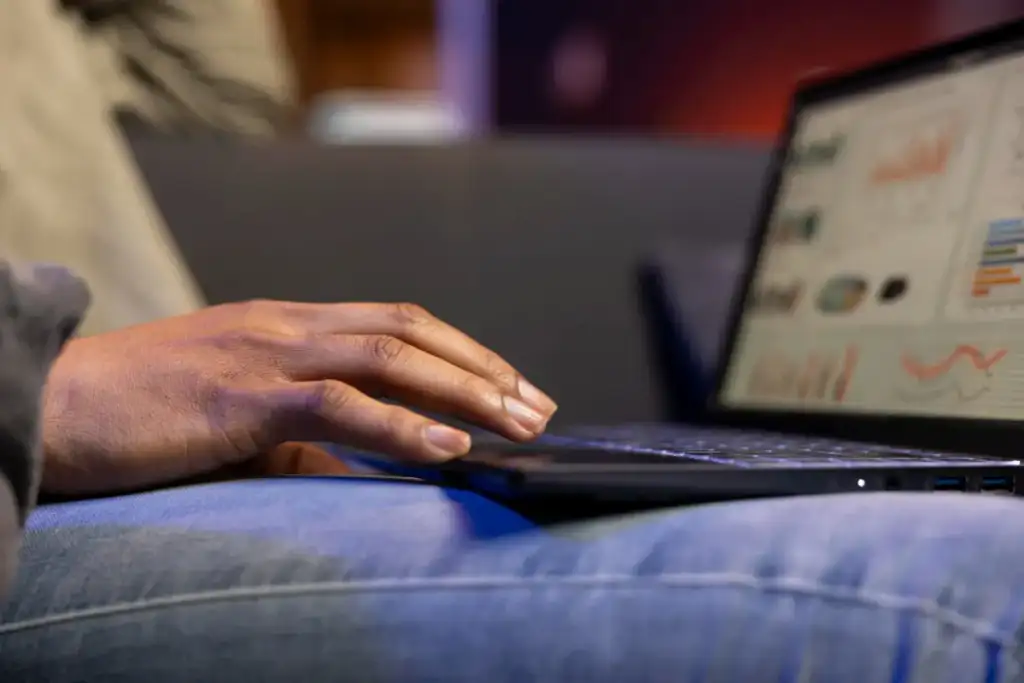 Pessoa usando notebook no colo, com gráficos e painéis de dados exibidos na tela