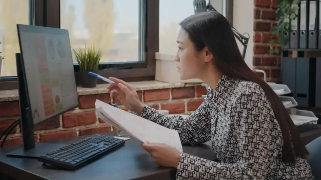 Mulher asiática comparando gráficos em papéis e computador, trabalhando para planejar o projeto de negócios no escritório de inicialização. Funcionário da empresa analisando documentos para projetar dados financeiros e estratégia.