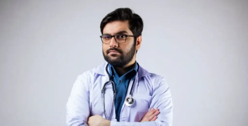 Médico homem com jaleco branco e estetoscópio no pescoço, de braços cruzados e expressão séria
