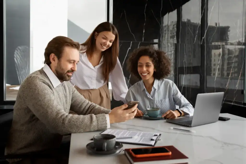 família olha para um celular em uma mesa de reunião com laptop e documentos