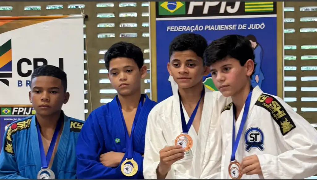 Quatro judocas jovens com medalhas ao pescoço, em pódio da Federação Piauiense de Judô, dois de kimono azul e dois de branco