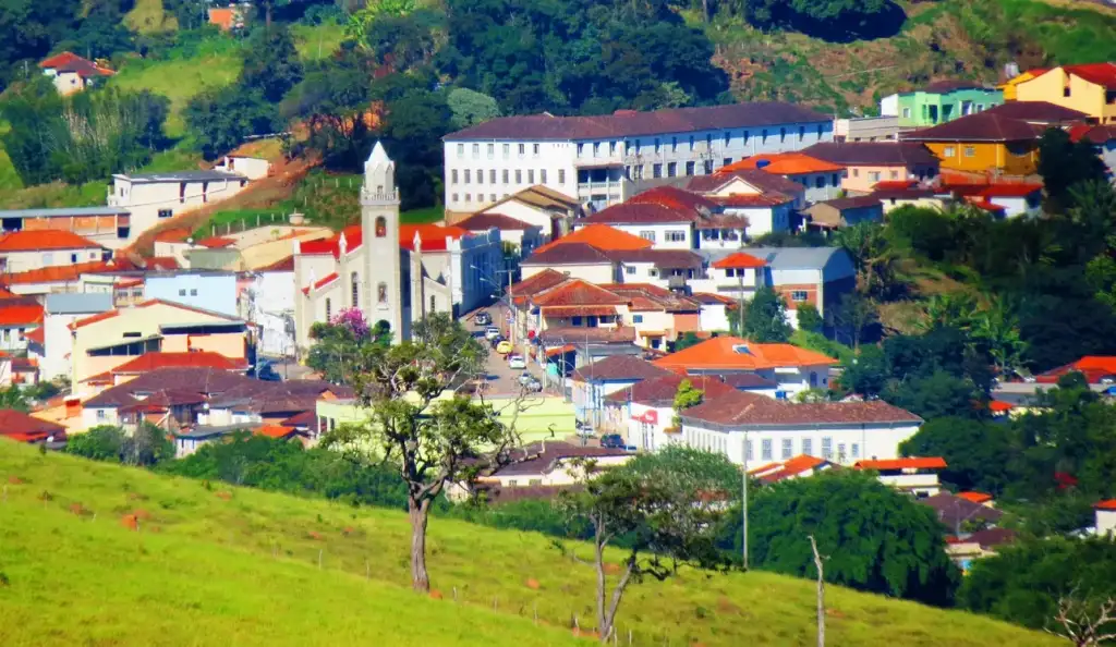 Vista aérea de Aiuruoca pequena cidade cercada por colinas verdes, com igreja de torre branca e casas de telhados coloridos