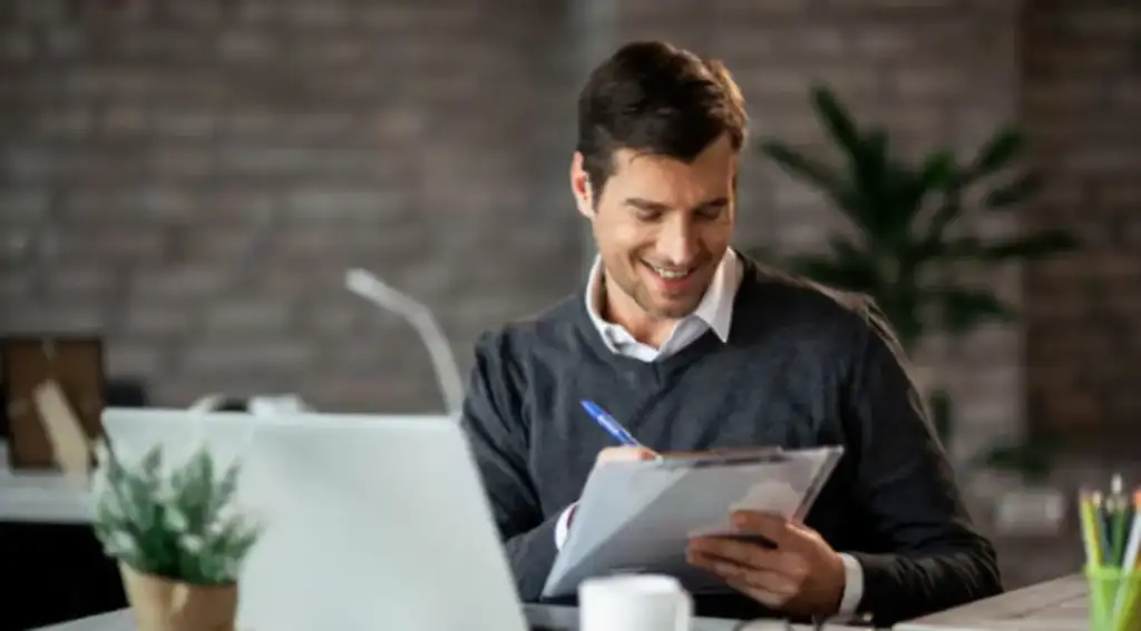 Homem sorridente escrevendo em uma prancheta enquanto trabalha em um escritório