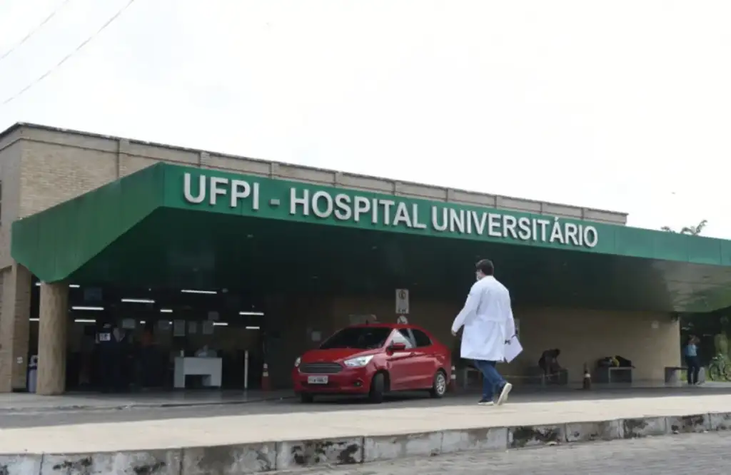 Fachada do Hospital Universitário da UFPI, com médico de jaleco caminhando na entrada