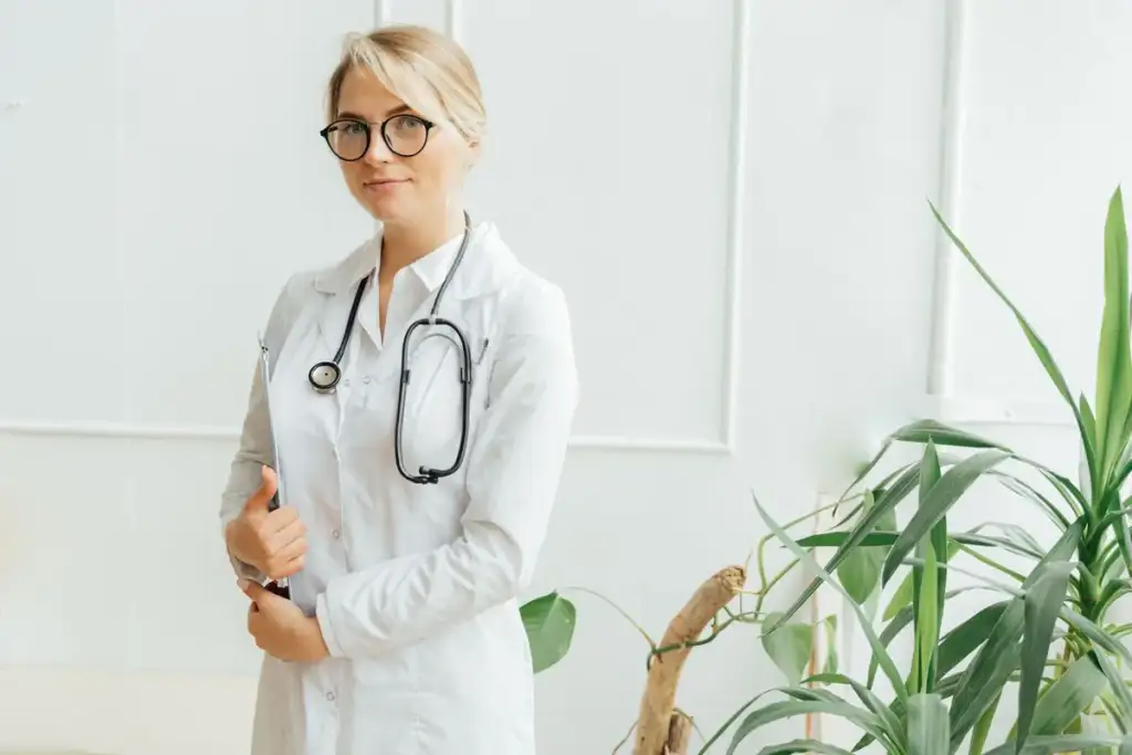 Médica de jaleco branco e estetoscópio segura uma prancheta ao lado de plantas