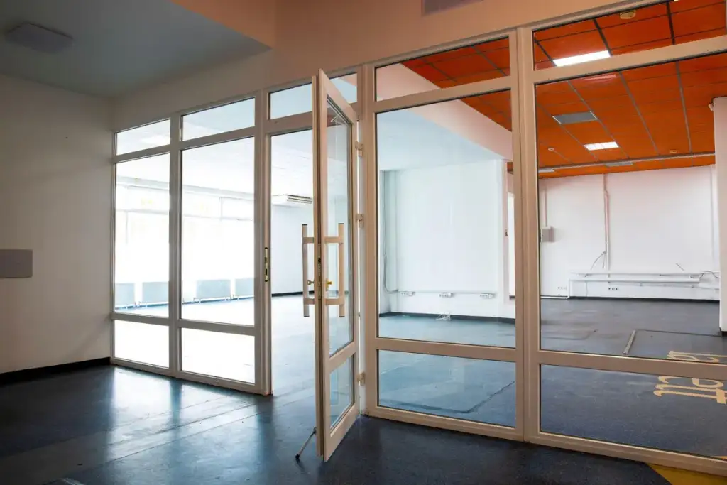 Sala comercial vazia com divisórias de vidro, porta aberta e teto laranja ao fundo