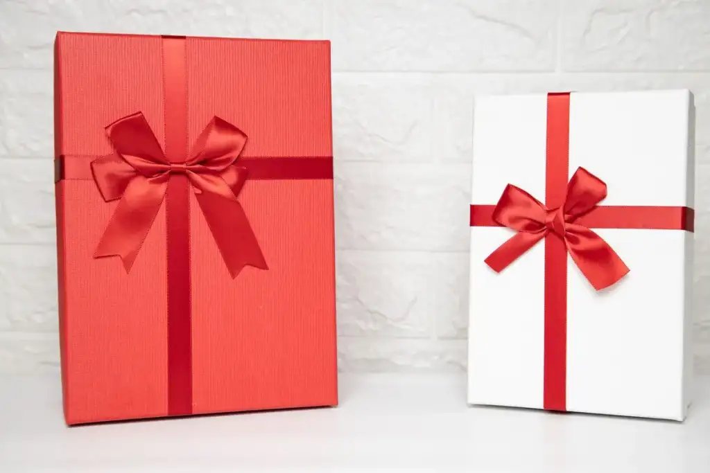 Duas caixas de presente, uma vermelha e outra branca, decoradas com laços de fita vermelha