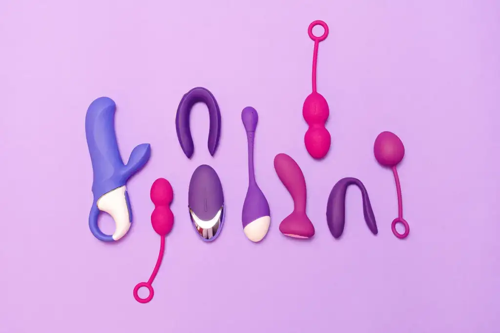 Sortimento de brinquedos sexuais em tons de roxo, rosa e magenta, organizados sobre fundo lilás