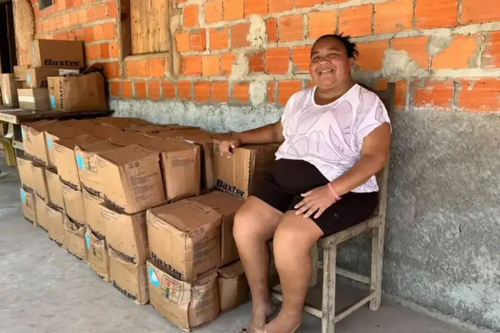 Mulher sorridente sentada ao lado de várias caixas de insumos empilhadas